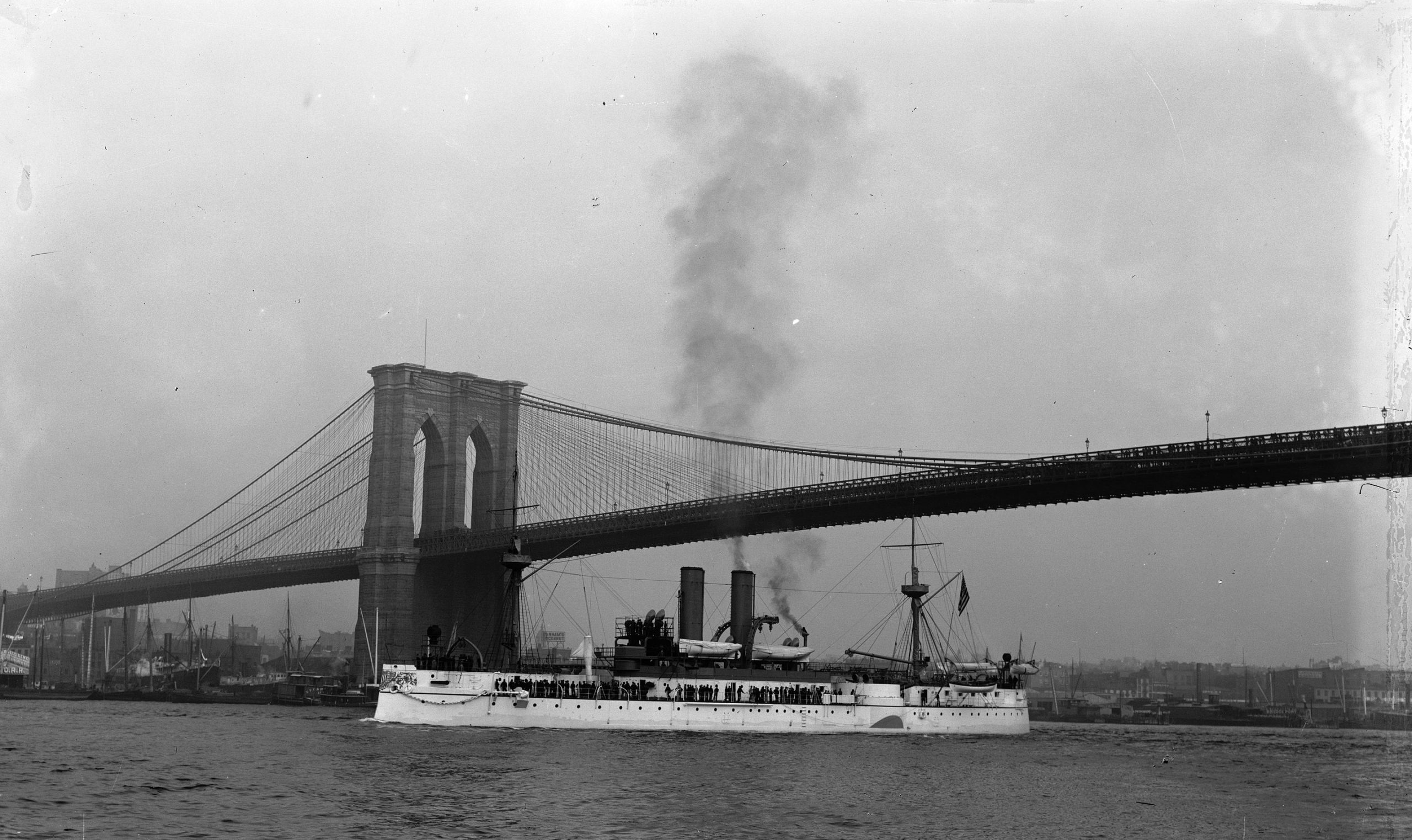 The USS Maine in better times, passing under the Brooklyn Bridge