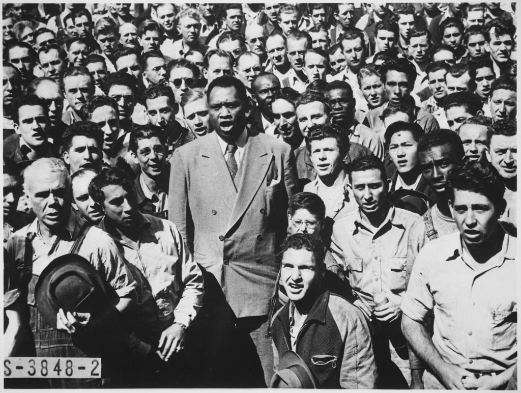 “Larger than life,” a physical giant among men: the larger than life Paul Robeson leading workers in singing The Star-Spangled Banner at the Moore Shipyard in Oakland, California, September of 1942